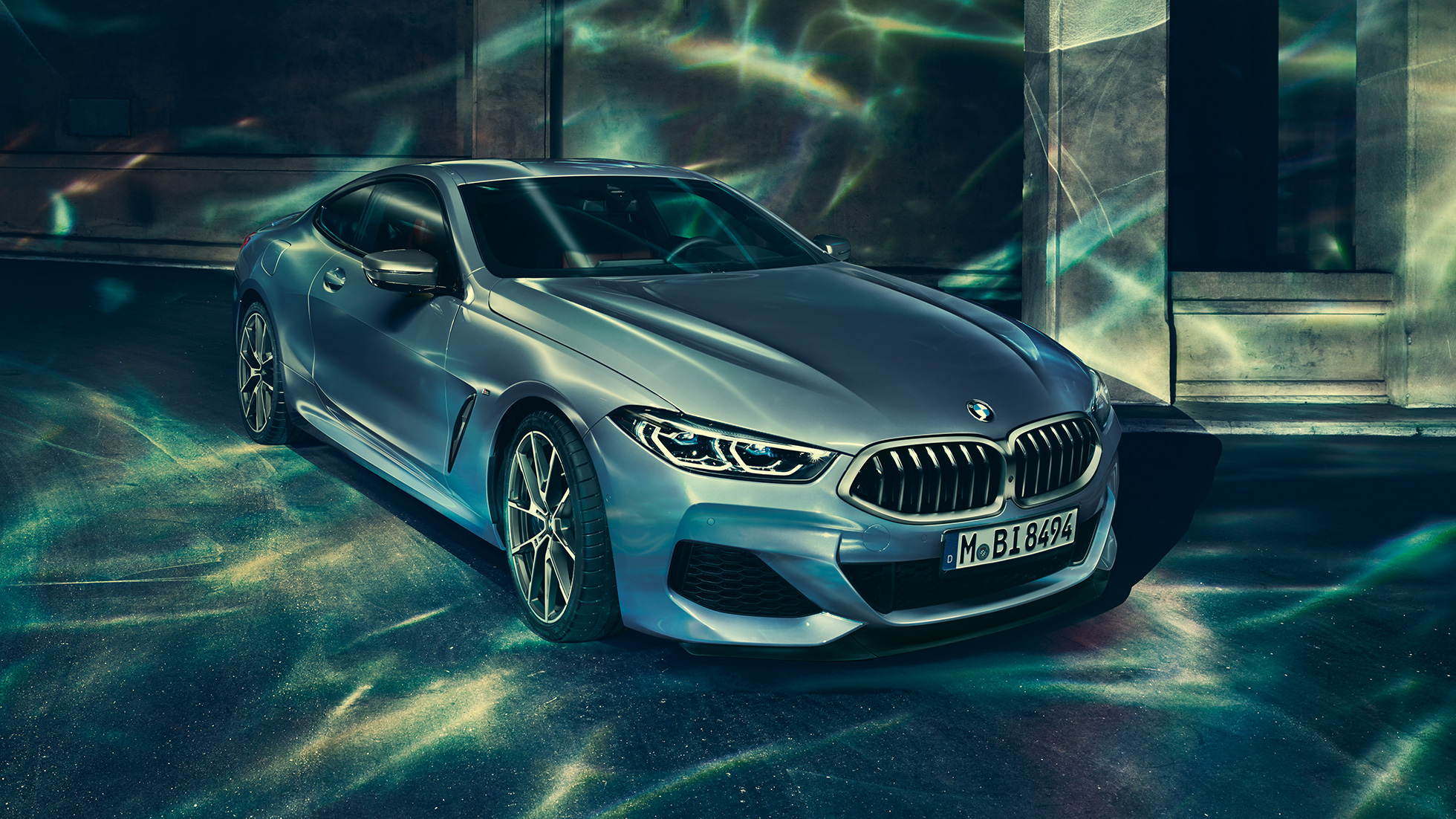 BMW M850i xDrive Coupé, háromnegyedes bal elölnézet. Egy épület előtt álló, Barcelona kék metálfényezésű BMW M850i xDrive Coupé háromnegyedes bal elölnézetből.