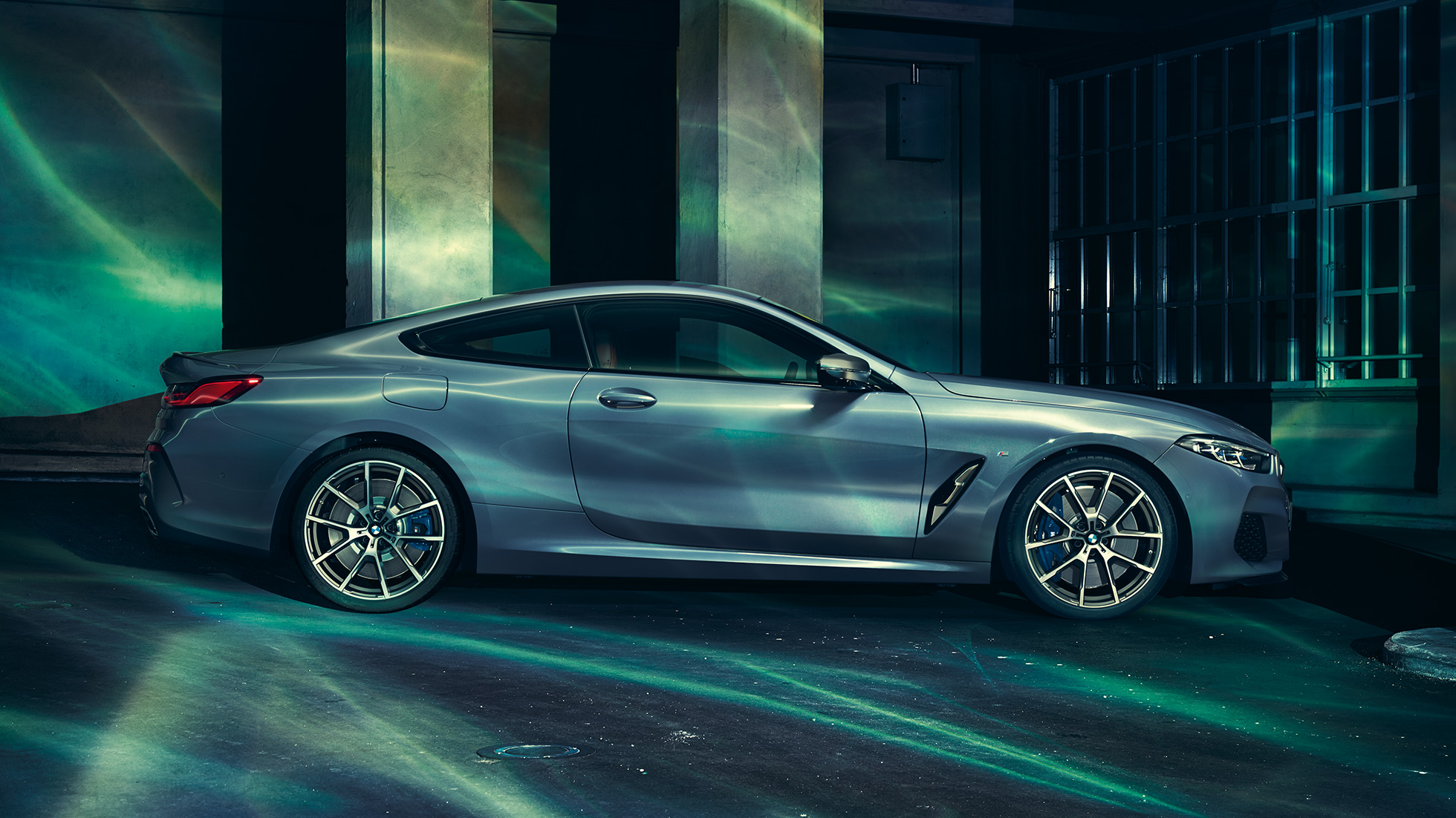 BMW M850i xDrive Coupé, oldalnézet. Egy épület előtt álló, Barcelona kék metálfényezésű BMW M850i xDrive Coupé oldalnézetből.