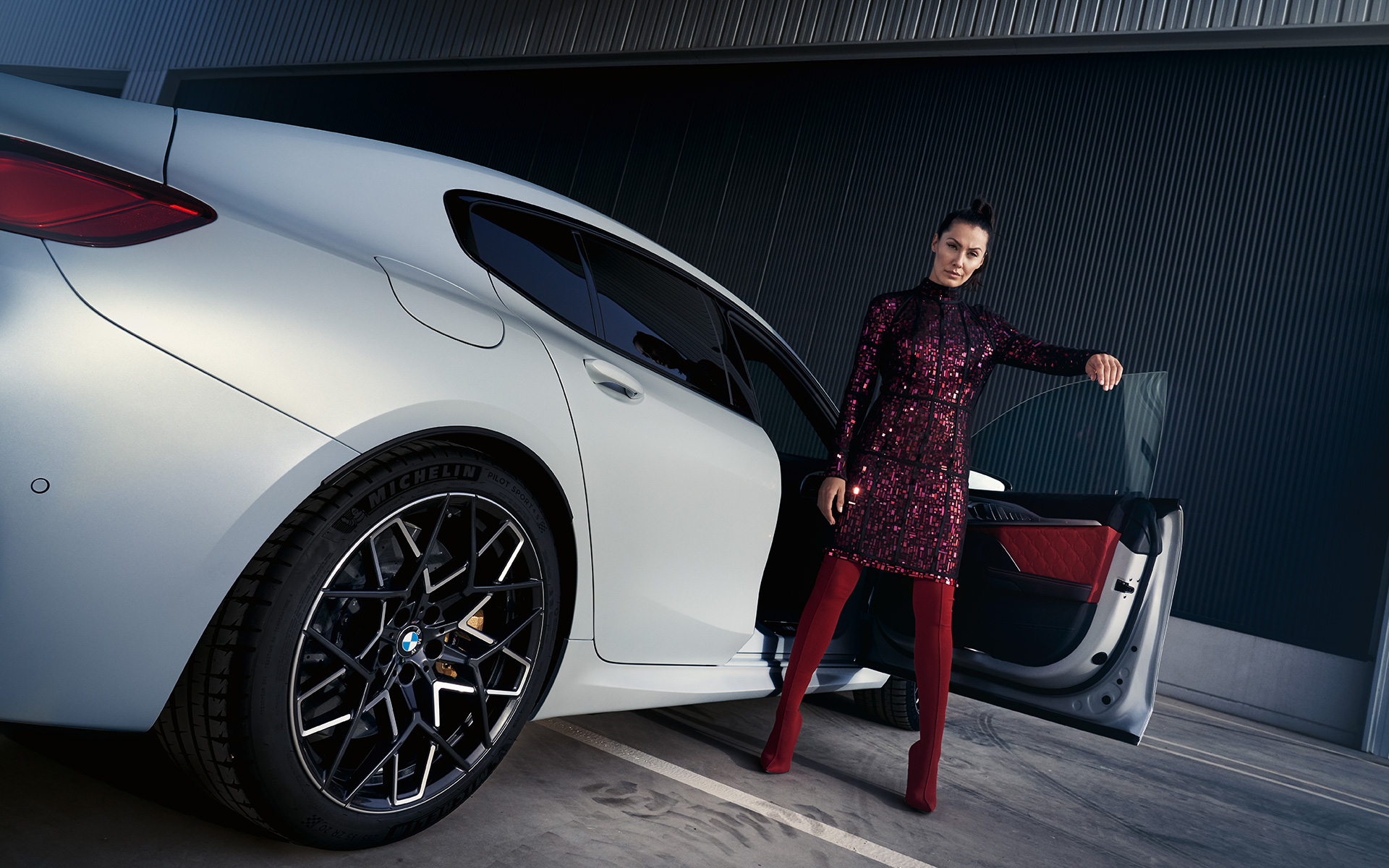 BMW M8 Competition Gran Coupé, F93 LCI, 2022, egy modell társaságában látható autó alulsó rézsútos hátulnézetből BMW M8 Competition Gran Coupé, F93 LCI, Facelift 2022, egy modell társaságában látható, BMW Individual Frozen briliáns fehér metálfényezésű autó alulsó rézsútos hátulnézetből
