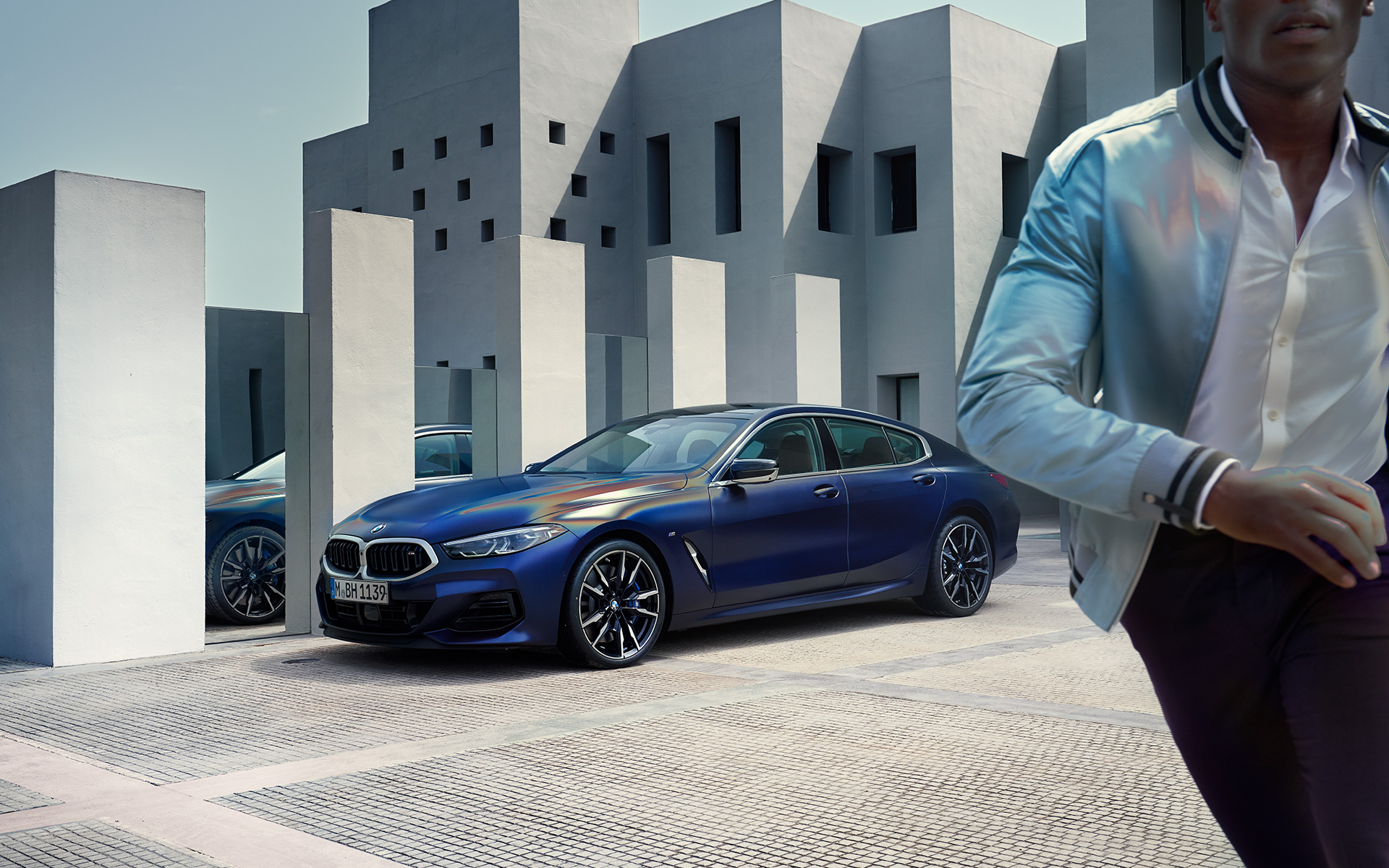 Rézsútos elölnézet, BMW M850i xDrive Gran Coupé, G16 LCI, Facelift 2022 BMW M850i xDrive Gran Coupé, G16 LCI, Facelift 2022, egy rézsútos elölnézetből látható BMW Individual Frozen Tanzanit kék metálfényezésű autó egy férfi modellel az előtérben