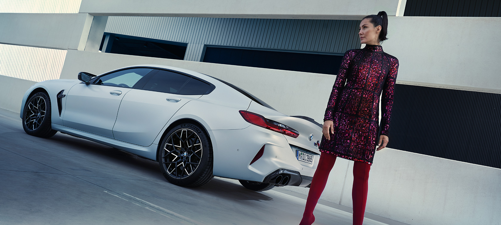 Rézsútos hátulnézet, BMW M8 Competition Gran Coupé, F93 LCI, 2022 BMW M8 Competition Gran Coupé, F93 LCI, Facelift 2022, egy női modell áll egy rézsútos hátulnézetből látható BMW Individual Frozen Briliáns fehér metálfényezésű autó mellett