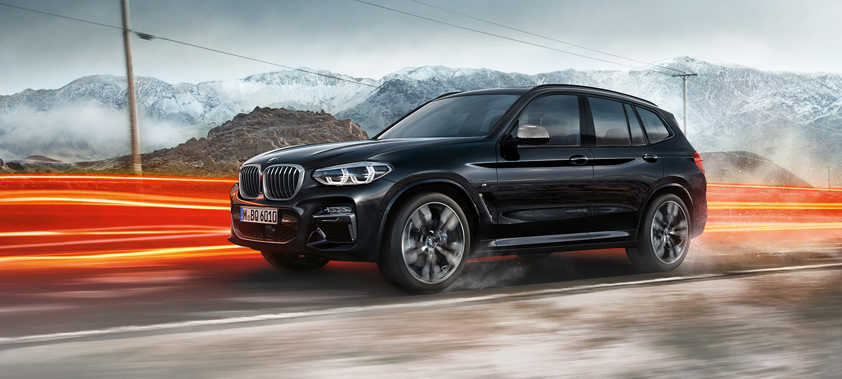 BMW X3 M40i és BMW X3 M40d, oldalnézet. Zafírfekete metálfényezésű BMW X3 M40i és BMW X3 M40d, menet közben, kívülről, oldalnézetből, hegyvidéki tájjal a háttérben, fénycsíkokkal.