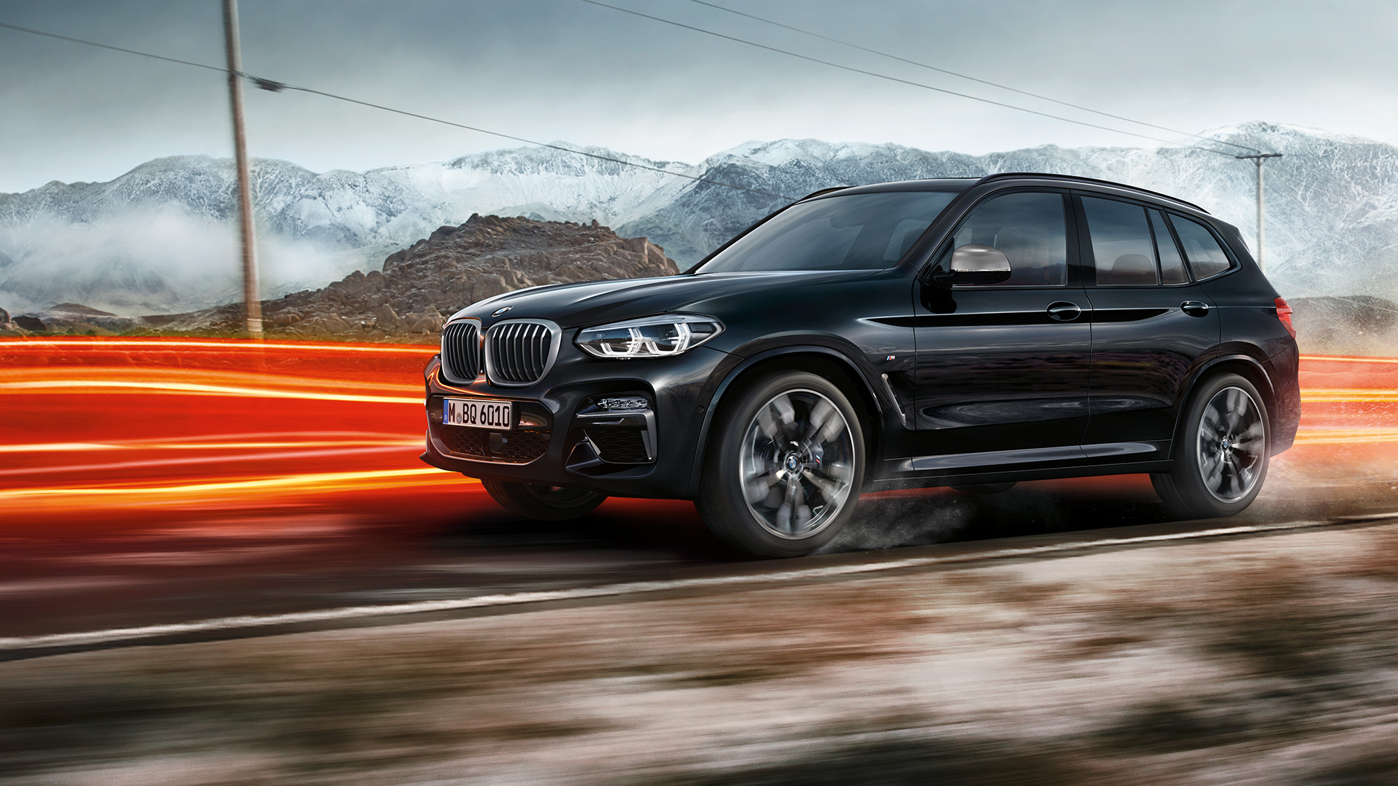 BMW X3 M40i és BMW X3 M40d, oldalnézet. Zafírfekete metálfényezésű BMW X3 M40i és BMW X3 M40d, menet közben, kívülről, oldalnézetből, hegyvidéki tájjal a háttérben, fénycsíkokkal.
