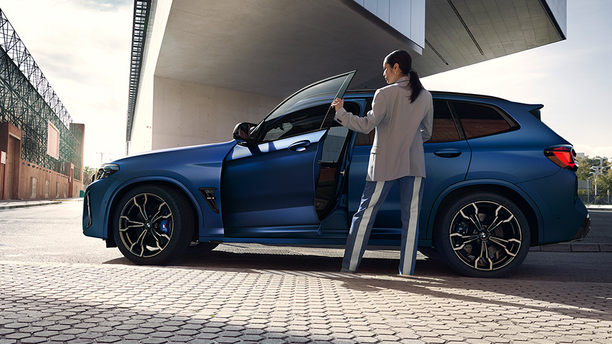 BMW X3 M Competition, F97 LCI, 2021, egy női modell társaságában látható, nyitott ajtajú autó oldalnézetből BMW X3 M Competition, F97 LCI, Facelift 2021, egy női modell társaságában látható, nyitott ajtajú, Frozen Marina Bay kék metálfényezésű autó oldalnézetből