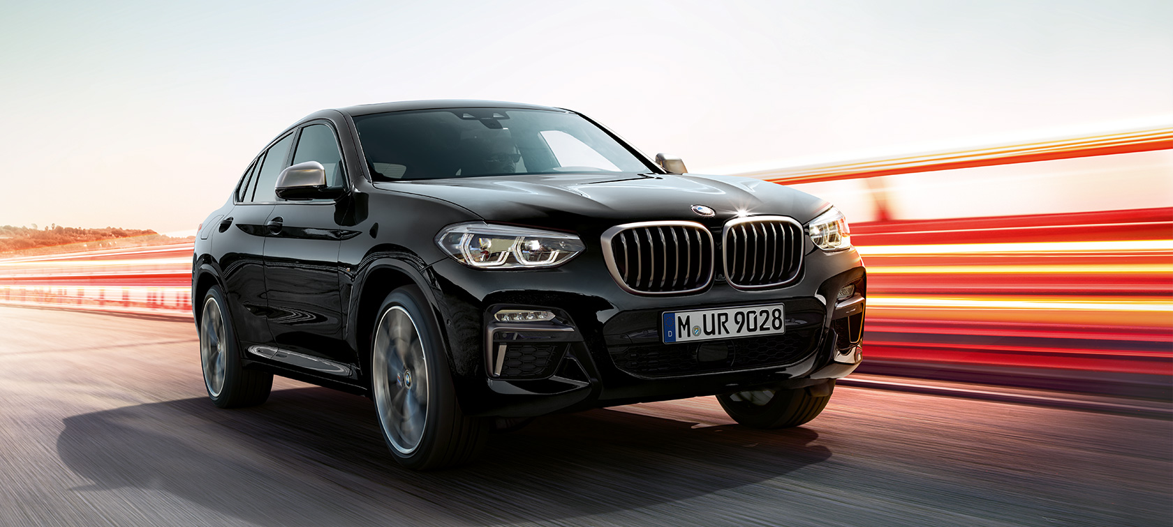 BMW X4 M40i és BMW X4 M40d, háromnegyedes elölnézet, bal oldal. Zafírfekete metálfényezésű BMW X4 M40i és BMW X4 M40d, kívülről, háromnegyedes elölnézetből, bal oldal, fénycsíkokkal.