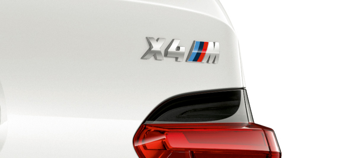 BMW X4 M, típusfelirat. Alpesi fehér BMW X4 M, kívülről, a far közelről a típusfelirattal.