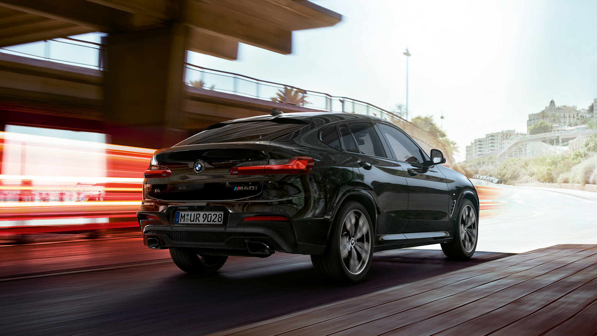 BMW X4 M40i, háromnegyedes elölnézet. Zafírfekete metálfényezésű BMW X4 M40i, menet közben, kívülről, háromnegyedes hátulnézetből, fénycsíkokkal.