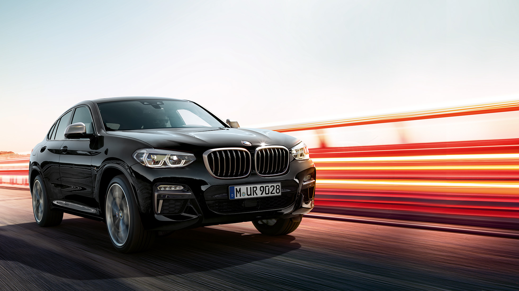 BMW X4 M40i, háromnegyedes hátulnézet. Zafírfekete metálfényezésű BMW X4 M40i, menet közben, kívülről, háromnegyedes hátulnézetből, fénycsíkokkal.