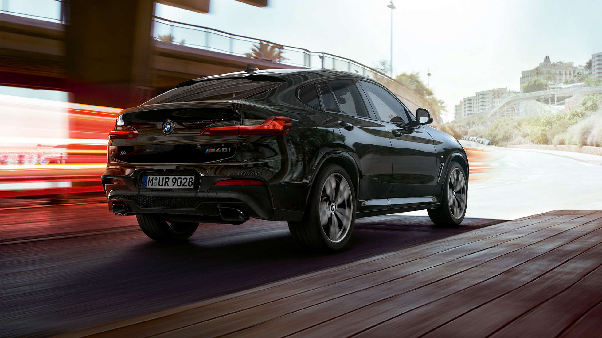 BMW X4 M40i, háromnegyedes hátulnézet. Zafírfekete metálfényezésű BMW X4 M40i, kívülről, háromnegyedes hátulnézetből, a jobb oldal fénycsíkokkal.