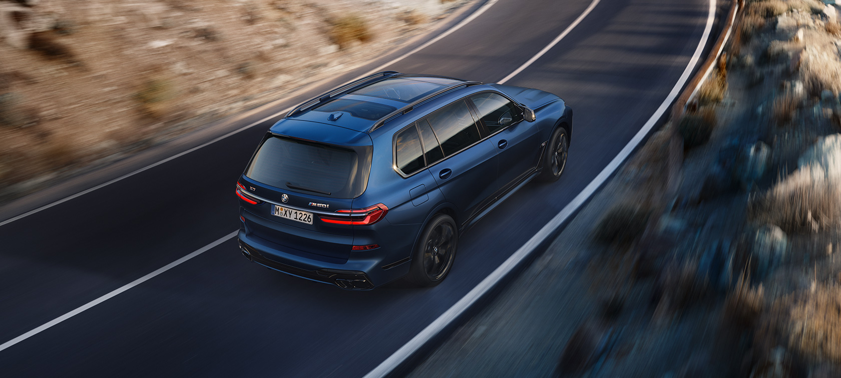 BMW X7 M60i xDrive, G07 LCI, egy utcán haladó, Frozen Marina Bay kék fényezésű autó rézsútos felülső hátulnézetből BMW X7 M60i xDrive, G07 LCI, egy utcán haladó, Frozen Marina Bay kék fényezésű autó rézsútos felülső hátulnézetből
