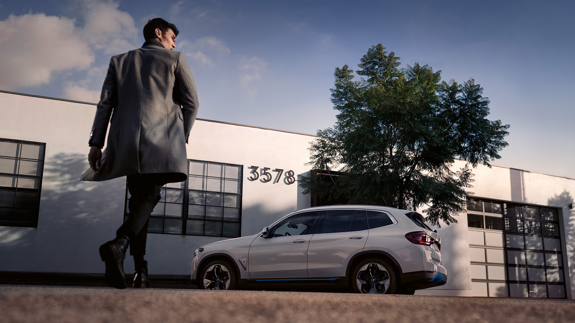 BMW iX3, G08, oldalnézet egy épület előtt, egy férfival BMW iX3, G08, 2020, egy épület előtt álló, Kristály fehér metálfényezésű autó oldalnézetből, egy férfival