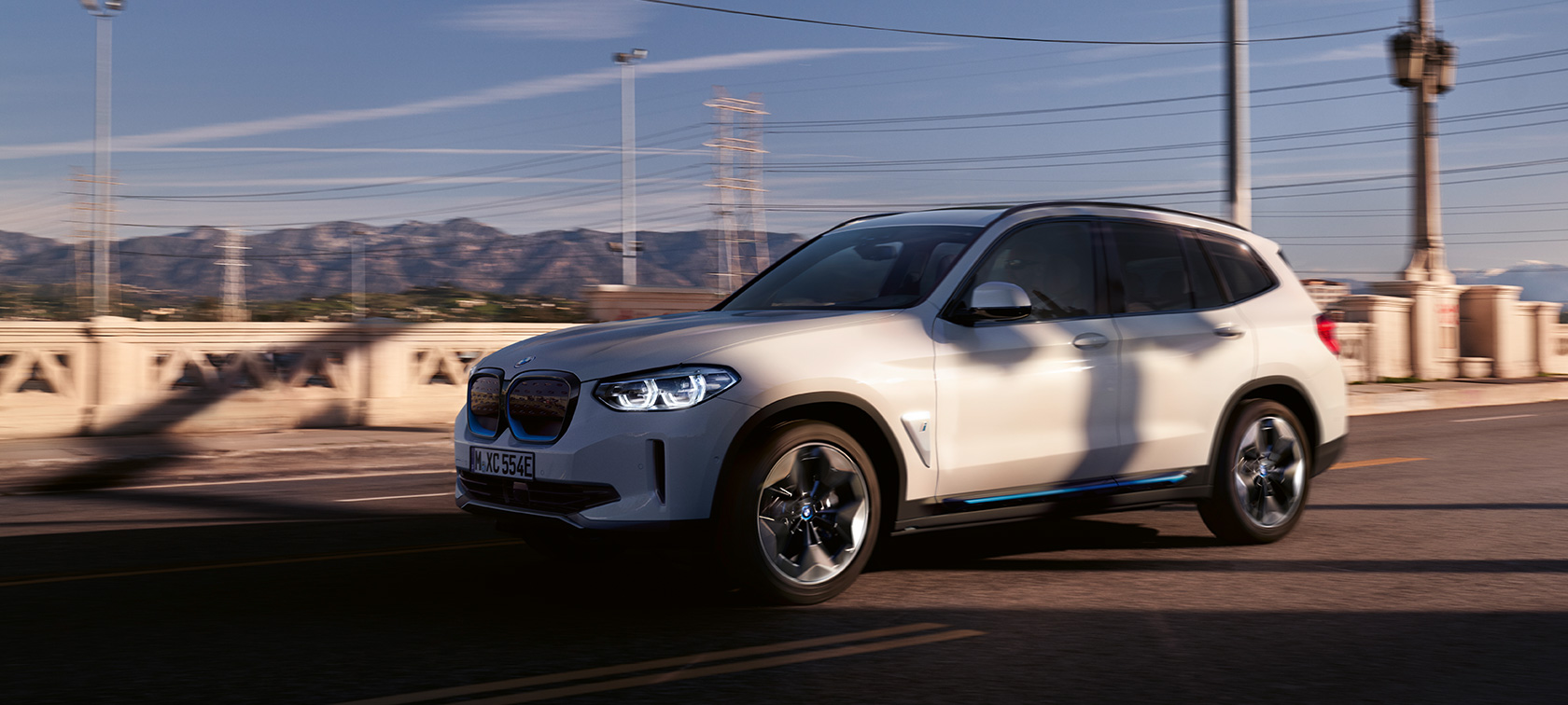 BMW iX3, G08, egy mozgó autó rézsútos elölnézetből BMW iX3, G08, 2020, egy úton haladó, Kristály fehér metálfényezésű autó rézsútos elölnézetből