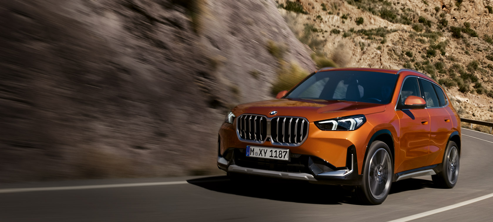 BMW X1, U11, xLine, egy vidéki úton haladó, Utah narancs metálfényezésű autó rézsútos elölnézetből