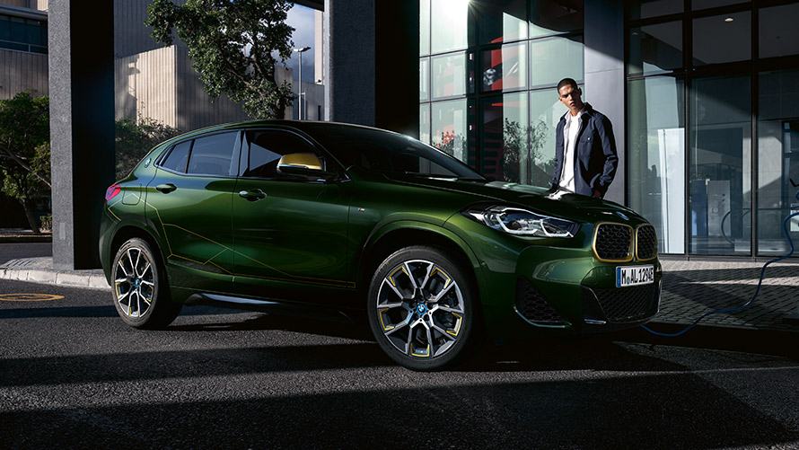 BMW X2, F39, egy modell társaságában látható, Sanremo zöld metálfényezésű autó rézsútos oldalnézetből BMW X2, F39, egy modell társaságában látható, Sanremo zöld metálfényezésű autó rézsútos oldalnézetből