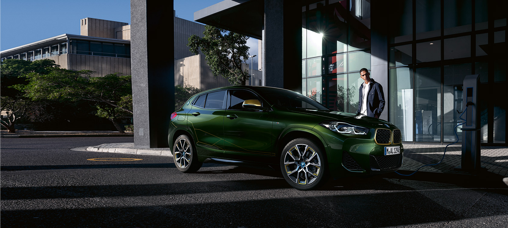 BMW X2, F39, egy modell társaságában látható, Sanremo zöld metálfényezésű autó rézsútos oldalnézetből BMW X2, F39, egy modell társaságában látható, Sanremo zöld metálfényezésű autó rézsútos oldalnézetből