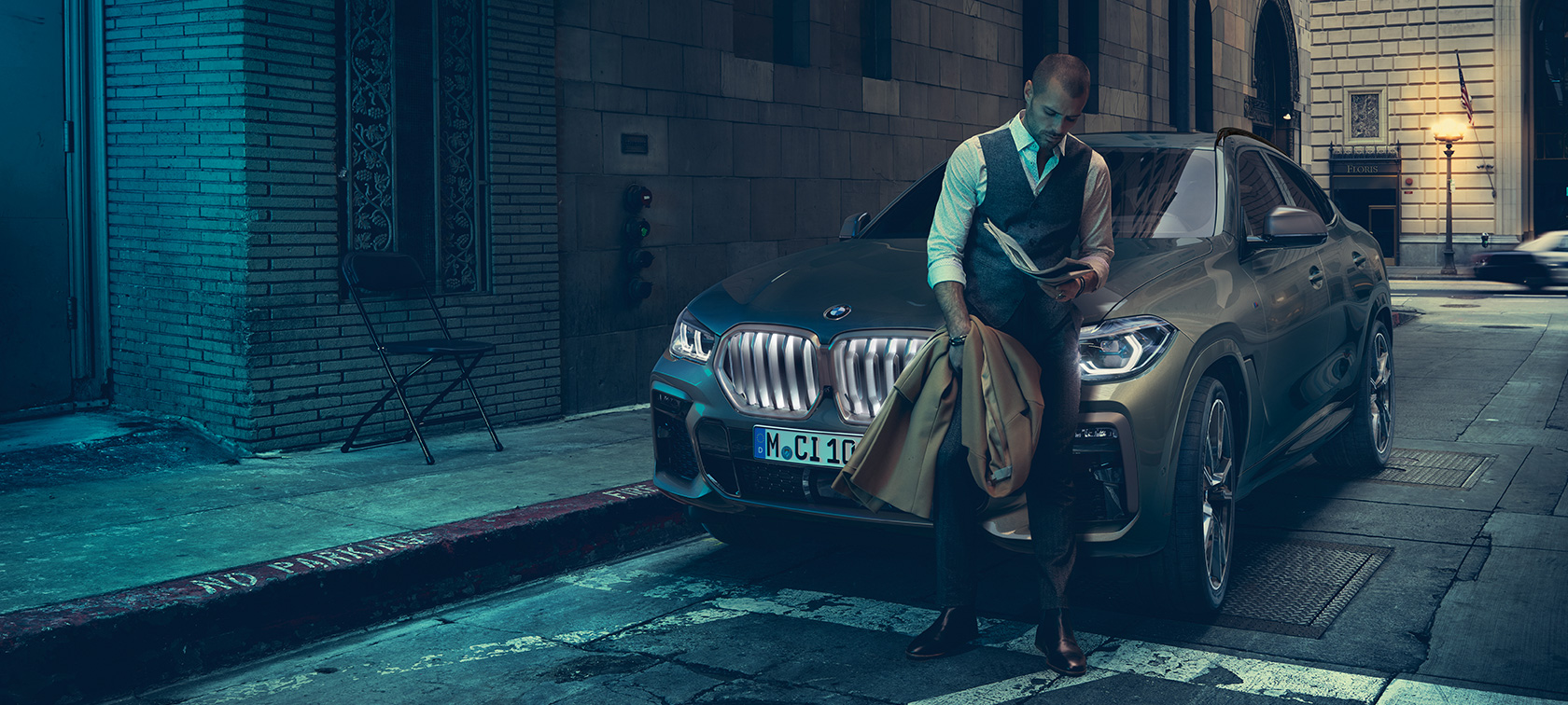 Egy férfi dől neki a BMW X6-nak. Egy férfi dől neki egy rézsútos elölnézetből látható, városi környezetben álló BMW X6-nak.
