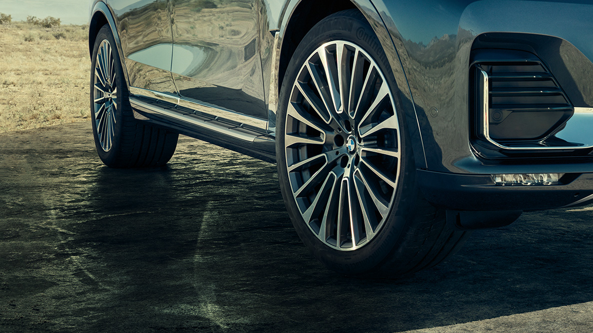 22” könnyűfém keréktárcsák 22” könnyűfém keréktárcsák: a BMW X7 háromnegyedes elölnézete a kerekekre fókuszálva