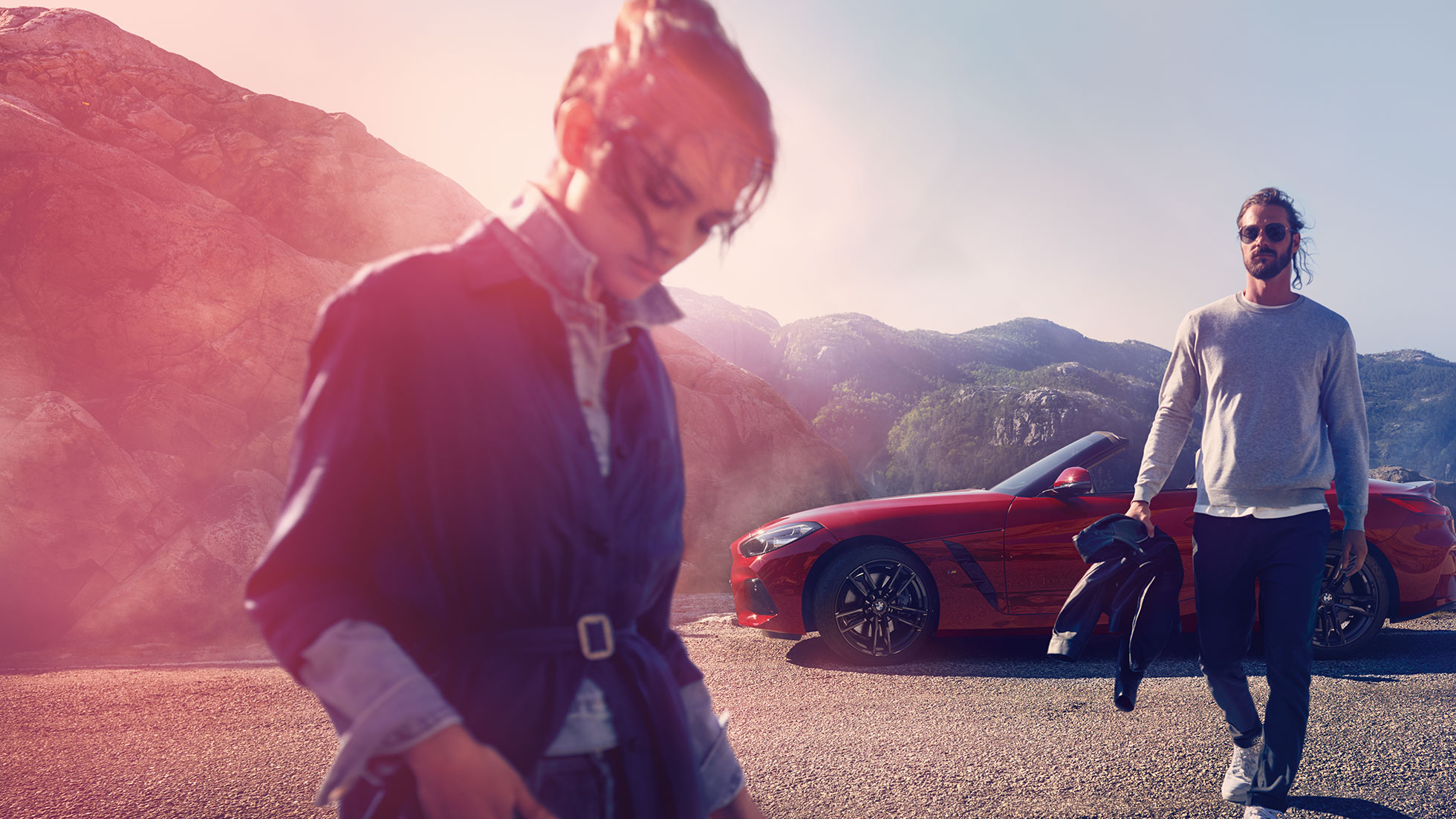 A BMW Z4 Roadster hegyekkel a háttérben Egy férfi és egy nő, valamint a BMW Z4 Roadster, hegyekkel a háttérben