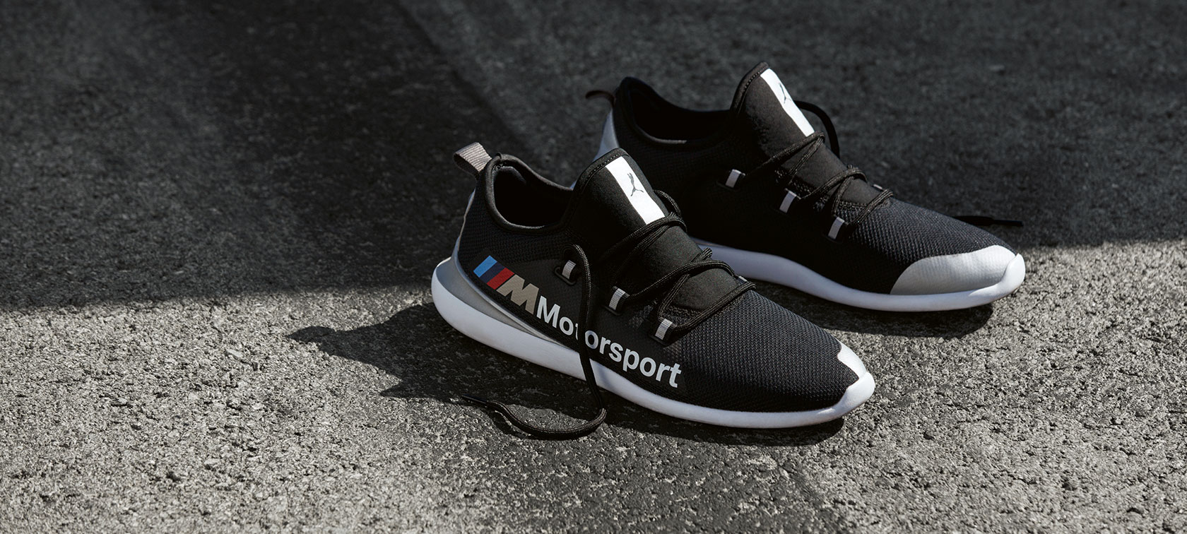 BMW M Motorsport PUMA EVO CAT cipő. A képen egy pár, a BMW M Motorsport Kollekcióba tartozó, aszfalton álló BMW M Motorsport PUMA EVO CAT cipő látható.