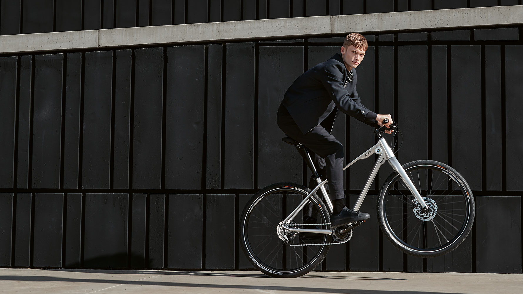 A képen egy fiatalember látható, aki egy BMW Cruise Bike-kal dinamikus egykerekezést hajt végre. A képen egy fiatalember látható, aki egy BMW Cruise Bike-kal dinamikus egykerekezést hajt végre.