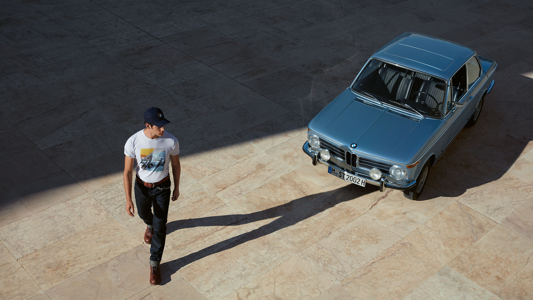 Egy BMW Classic férfipólót viselő férfi egy klasszikus BMW-t csodál. Egy BMW Classic férfipólót viselő férfi egy klasszikus BMW-t csodál.