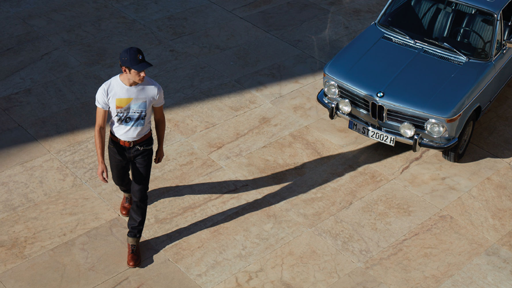 Egy BMW Classic férfipólót viselő férfi egy klasszikus BMW-t csodál. Egy BMW Classic férfipólót viselő férfi egy klasszikus BMW-t csodál.