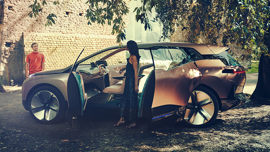 A BMW Vision iNEXT oldalnézetből A BMW Vision iNEXT profilból, egy nővel a nyitott ajtók mellett, a háttérben egy férfi