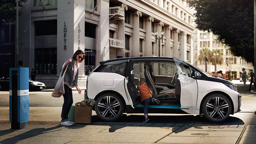 Egy BMW i3 városi városi környezetben BMW modellkínálat, egy BMW i3 városi környezetben egy nő és egy gyermek társaságában