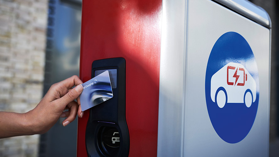 Nyilvános töltés a BMW Charging Card kártyával Egy személy egy BMW Charging Card kártyát tart a kezében egy nyilvános töltőállomáson