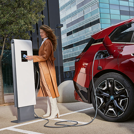 BMW iX, i20, SUV, egy BMW Charging kártyát a kezében tartó nő egy töltőállomásnál