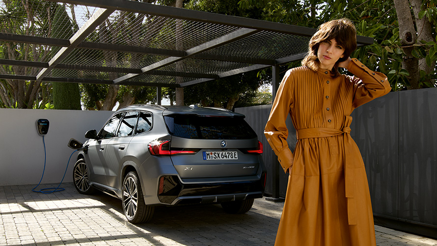 BMW X1 plug-in hibrid, 2022, U11, egy hátulnézetből látható autó egy modell társaságában BMW X1 plug-in hibrid, 2022, U11, egy hátulnézetből látható autó egy modell társaságában
