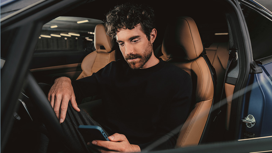 Egy BMW-ben ülő férfi Egy, a BMW-jében ülő, az okostelefonját néző férfi