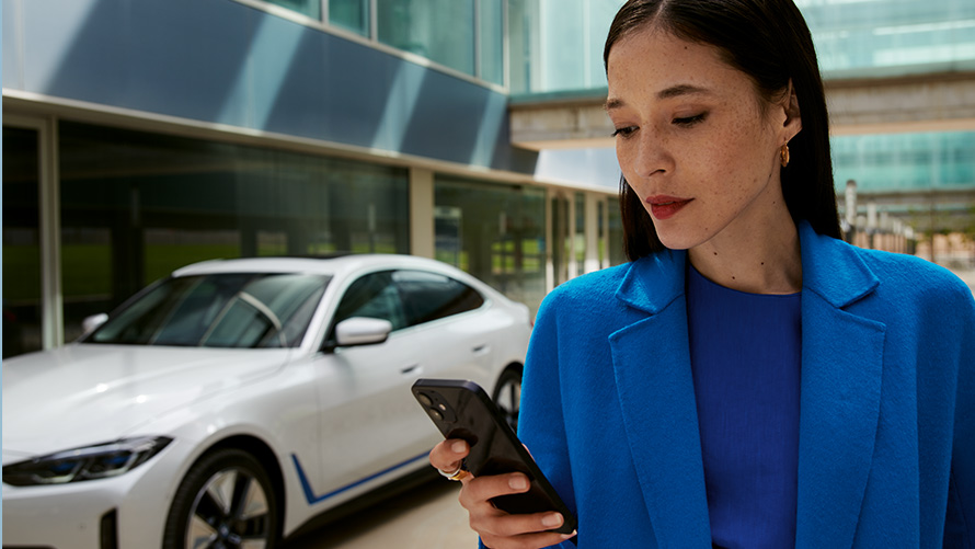 Egy, a BMW-je előtt álló nő Egy, a BMW-je előtt álló nő az okostelefonját nézi