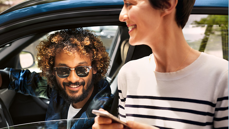 BMW Connected Egy, a BMW-ben ülő férfi, valamint egy, a BMW-n kívül lévő nő, aki a BMW Connected alkalmazást használja az okostelefonján