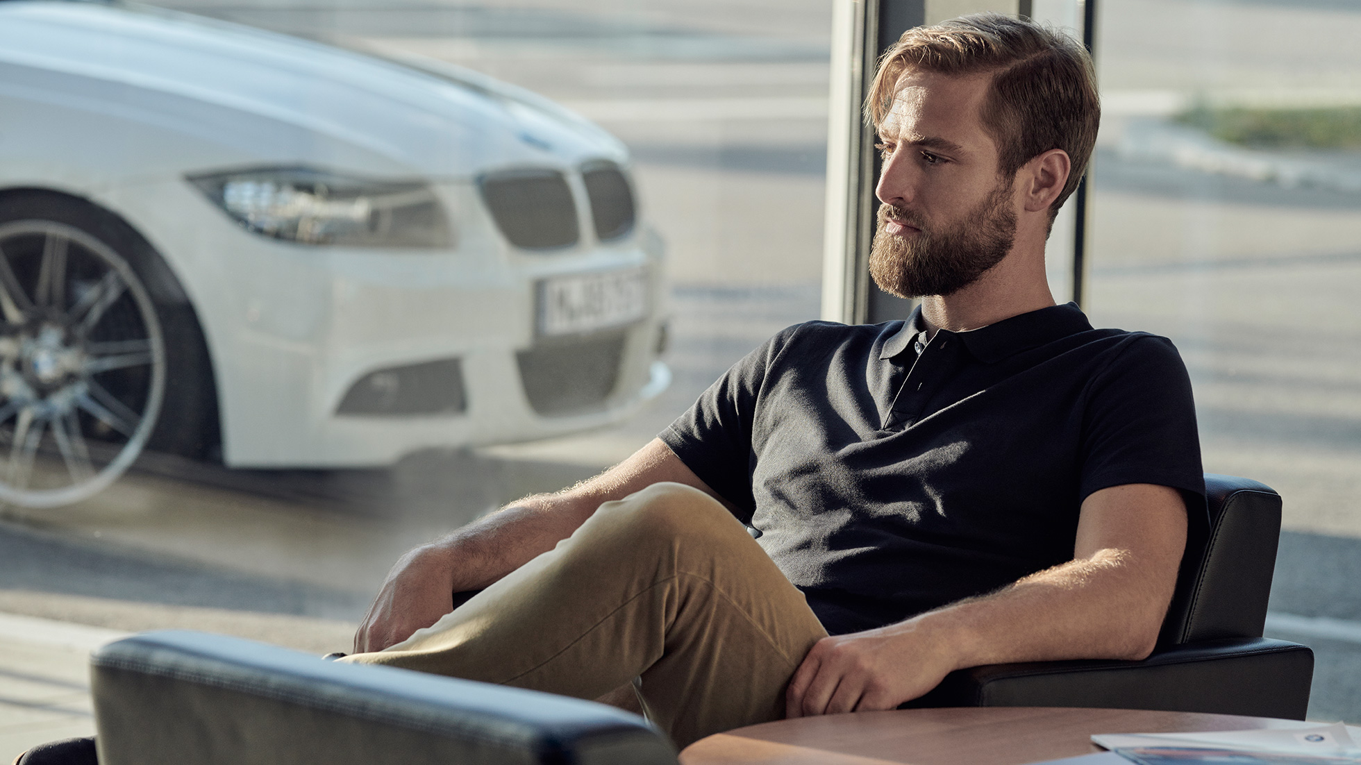 BMW Service, BMW Service Inclusive BMW Service, BMW Service Inclusive, egy fesztelenül nyugodt férfi ül egy BMW márkakereskedésben