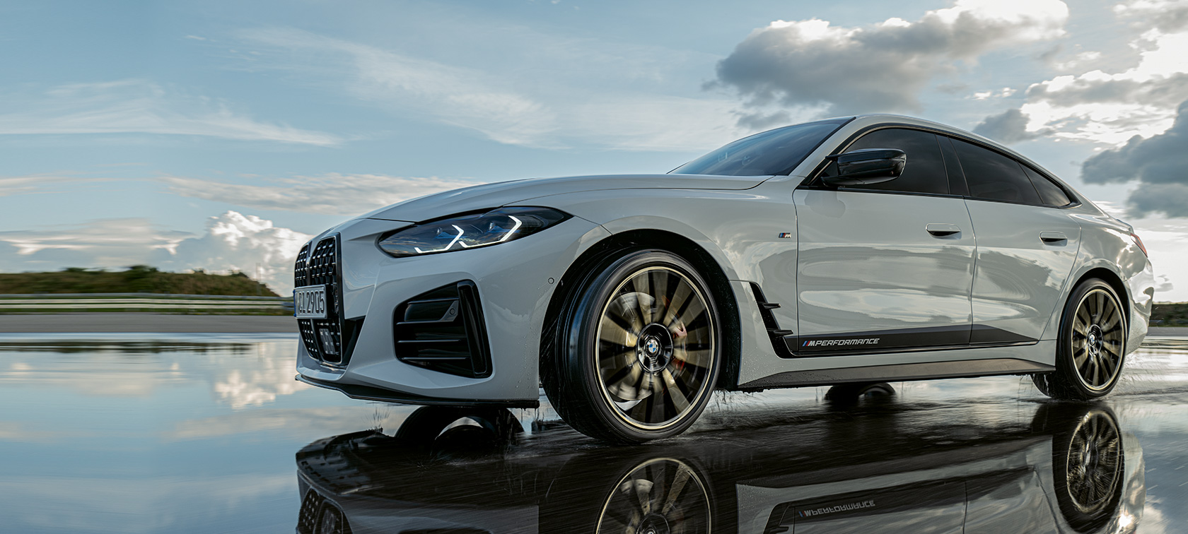 Egy vizes úton haladó, M Performance Parts tartozékokkal felszerelt BMW 4 Gran Coupé (G26) Egy vizes úton haladó, M Performance Parts tartozékokkal felszerelt BMW 4 Gran Coupé (G26)