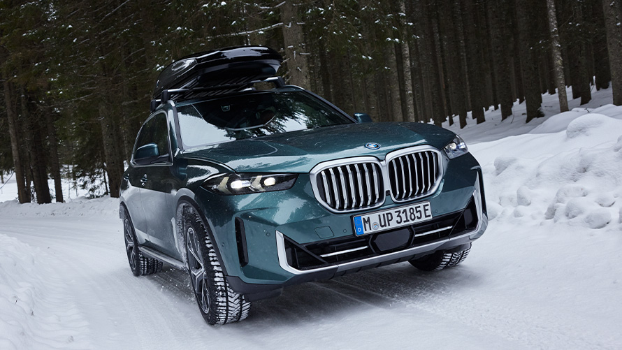 Komplett BMW téli kerekek egy havas erdei úton látható BMW X5 (G05 LCI) modellen Komplett BMW téli kerekek egy havas erdei úton látható BMW X5 (G05 LCI) modellen