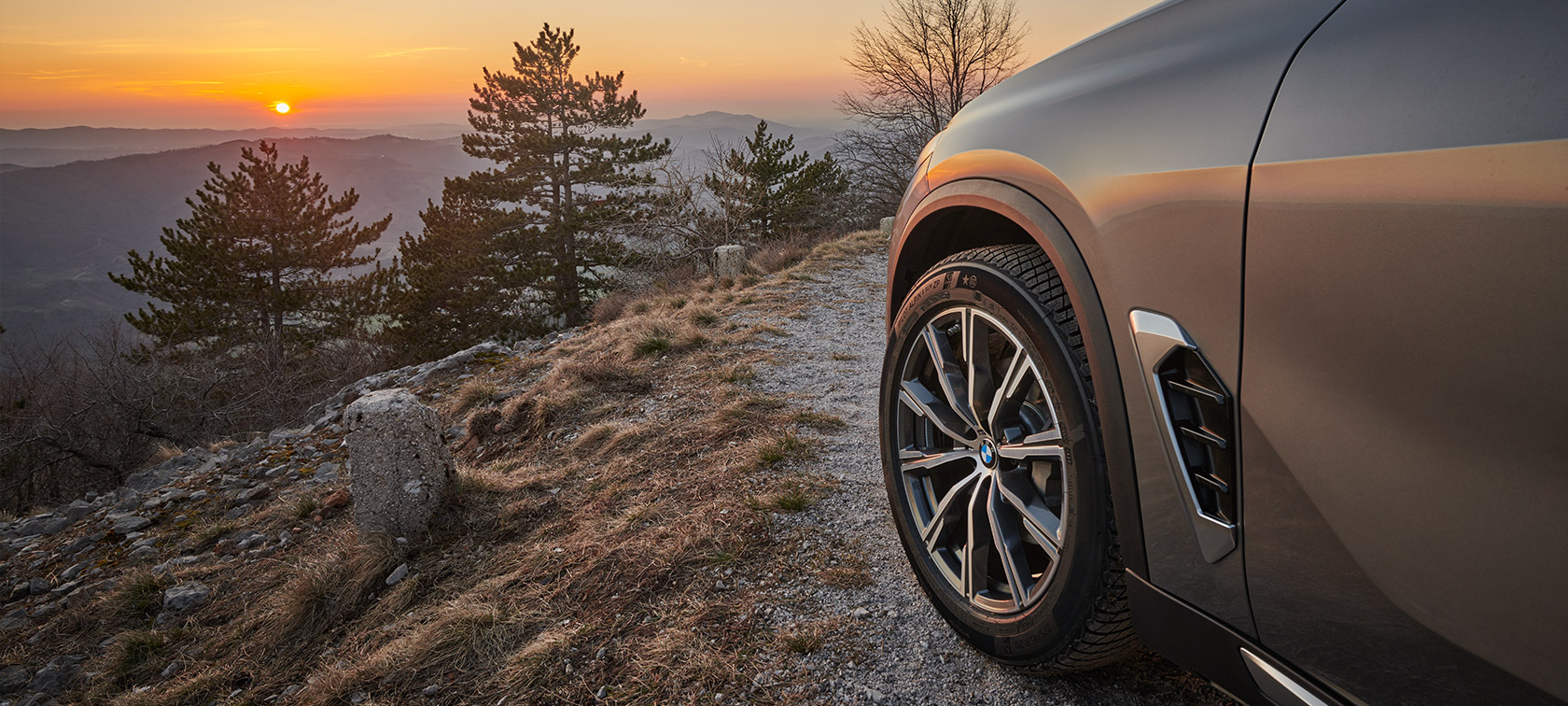 Eredeti BMW keréktárcsák egy BMW X5 (G05 LCI) modellen Eredeti BMW keréktárcsák egy hegyi földúton látható BMW X5 (G05 LCI) modellen, szemben a naplementével