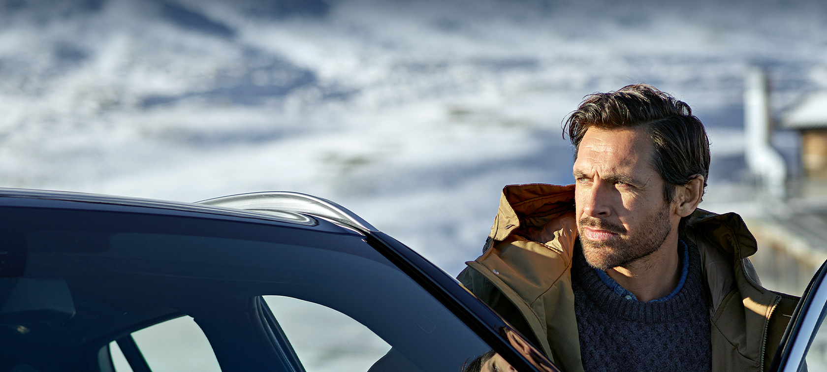 Eredeti BMW tartozékok és BMW Service szolgáltatások őszre és télre Egy téli anorákot viselő férfi áll BMW-je ajtója előtt