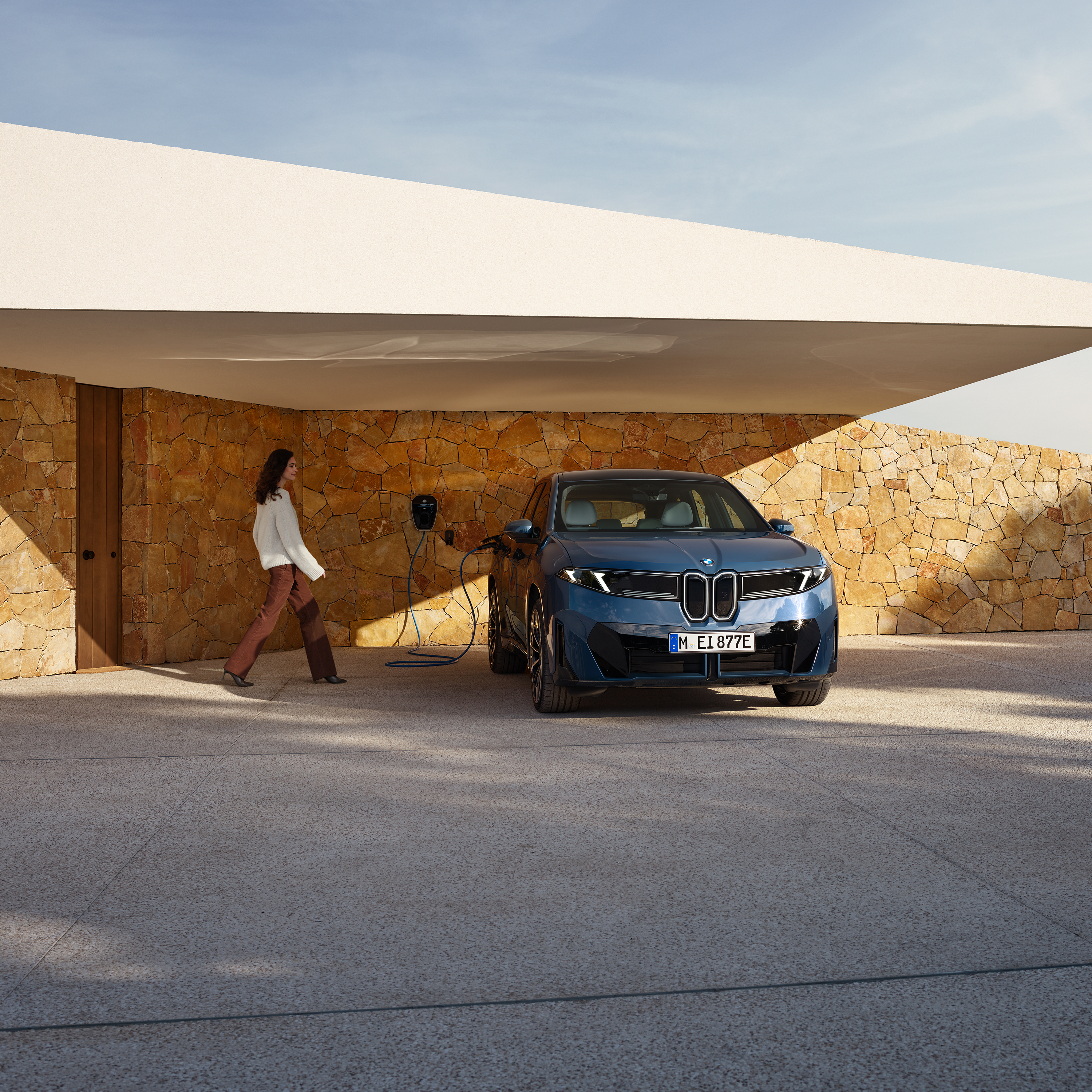 Egy nő egy Wallboxhoz csatlakoztatott BMW iX3 felé közeledik