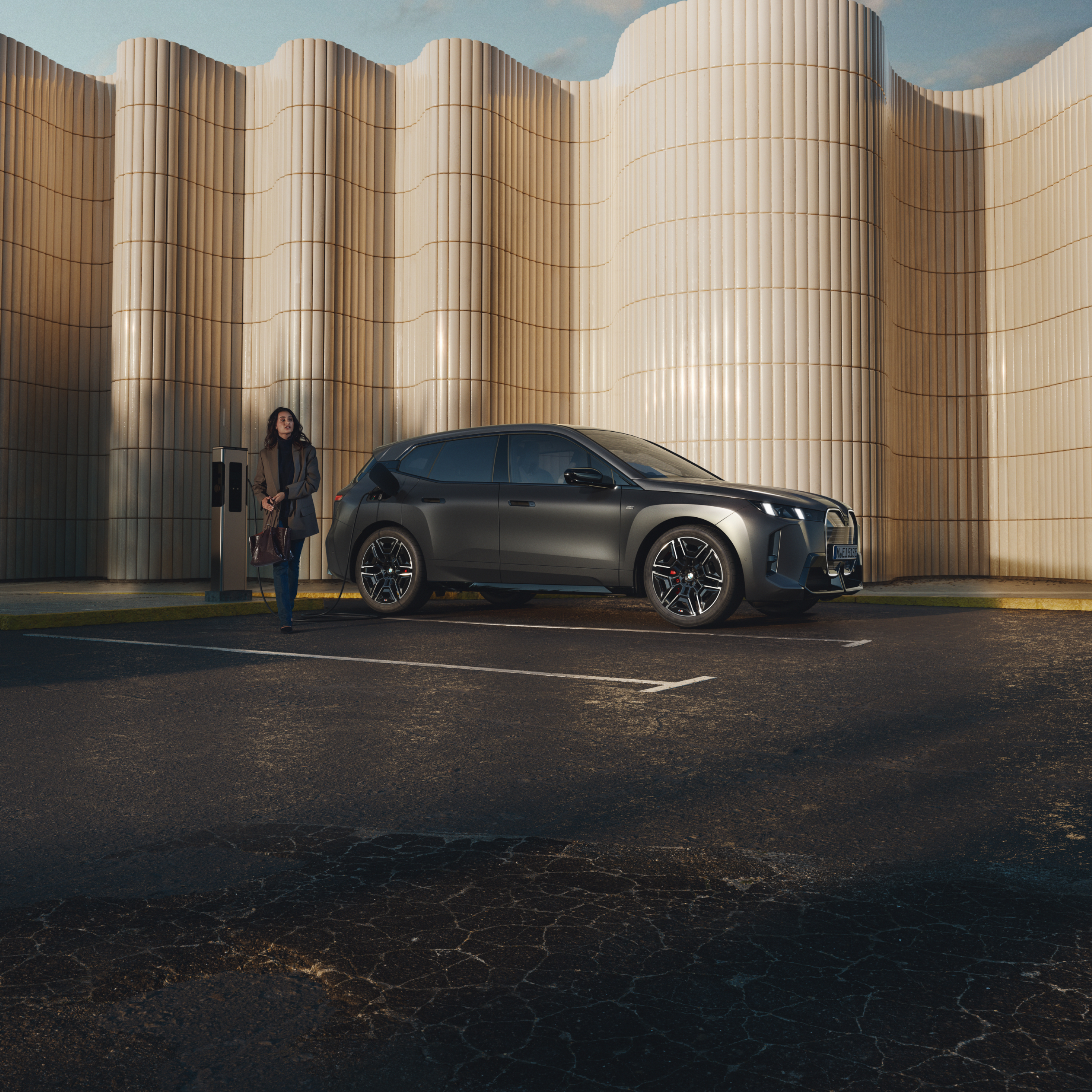 Egy BMW-re támaszkodó személy az út szélén lévő nyilvános elektromos töltőállomáson
